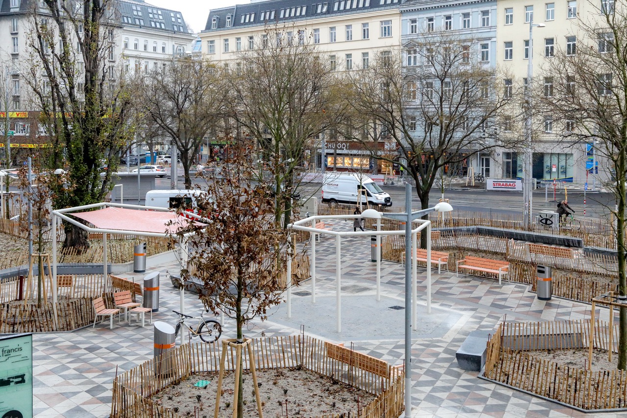 Julius-Tandler-Platz Aufnahme des neugestalteten Julius-Tandler-Platz mit heller Pflasterung, Begrünung, Beschattung und Sitzgelegenheiten